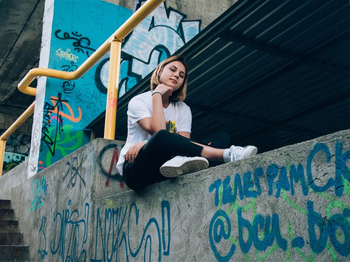 Ein junges Mädchen sitzt auf einer Graffiti besprühten Mauer und schaut lässig in die Kamera