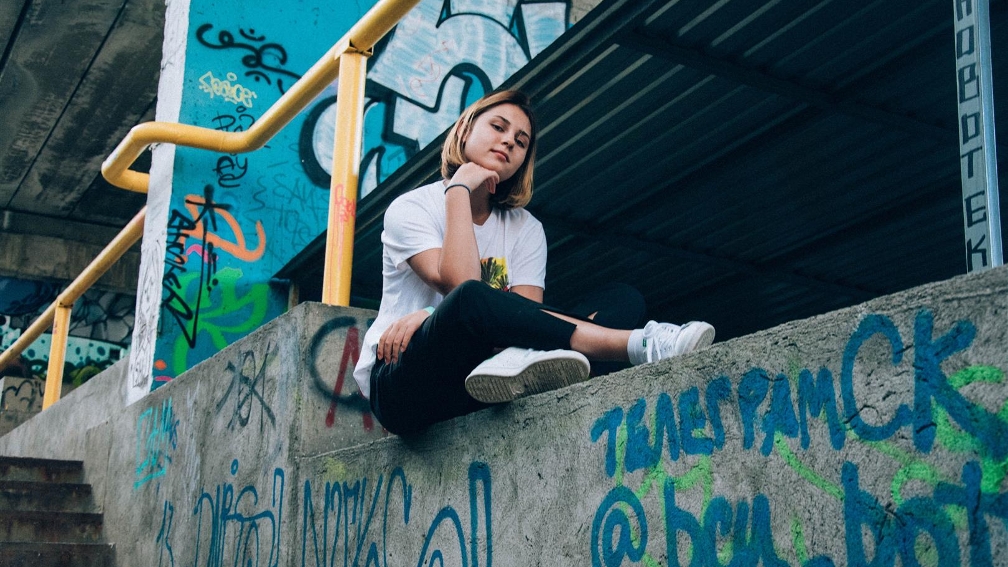 Ein junges Mädchen sitzt auf einer Graffiti besprühten Mauer und schaut lässig in die Kamera