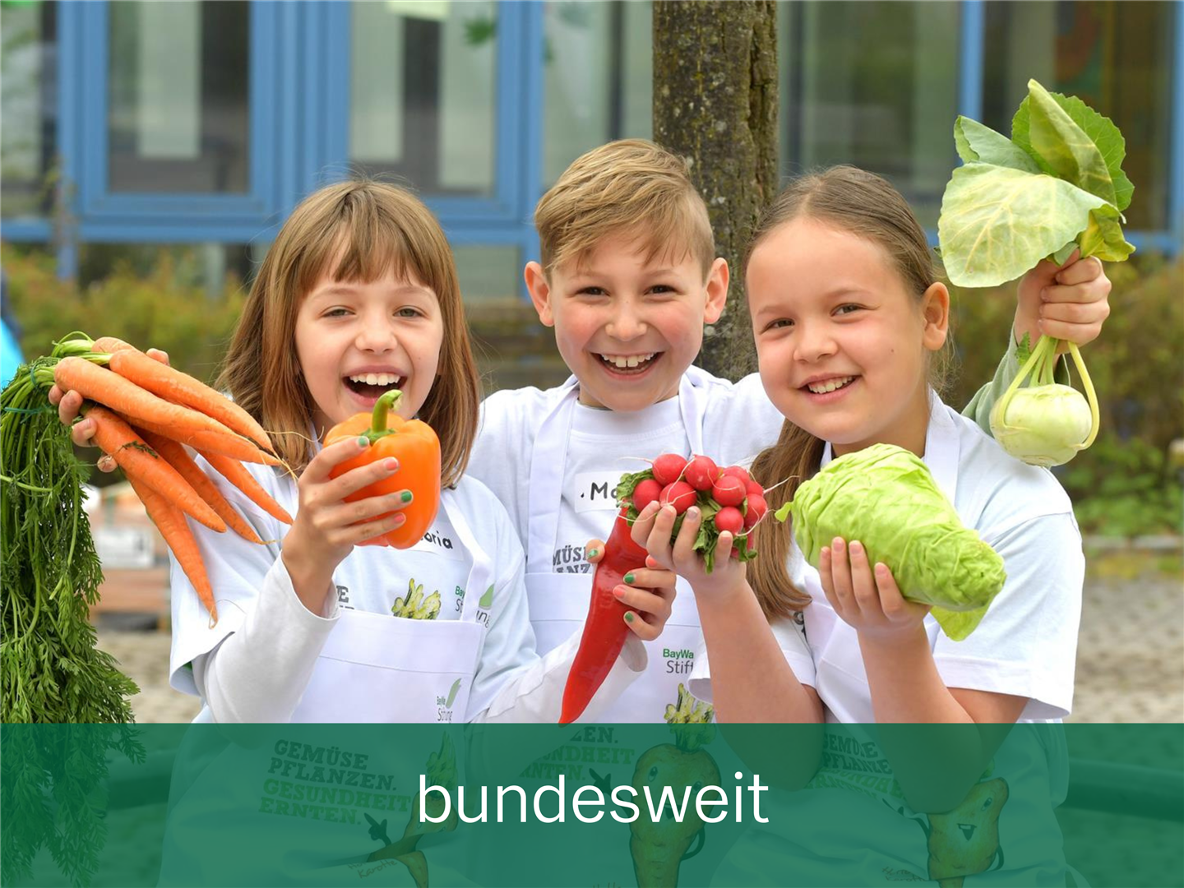Drei Schulkinder stehen mit selbstgeerntetem Gemüse in den Händen nebeneinander.