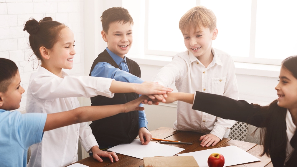Kinder, die an einem Tisch in die Hände einschlagen